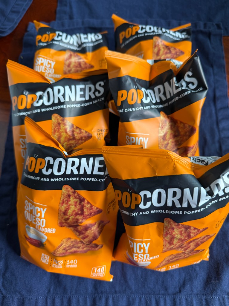Five bags of PopCorners Spicy Queso snack, stacked on a blue cloth.