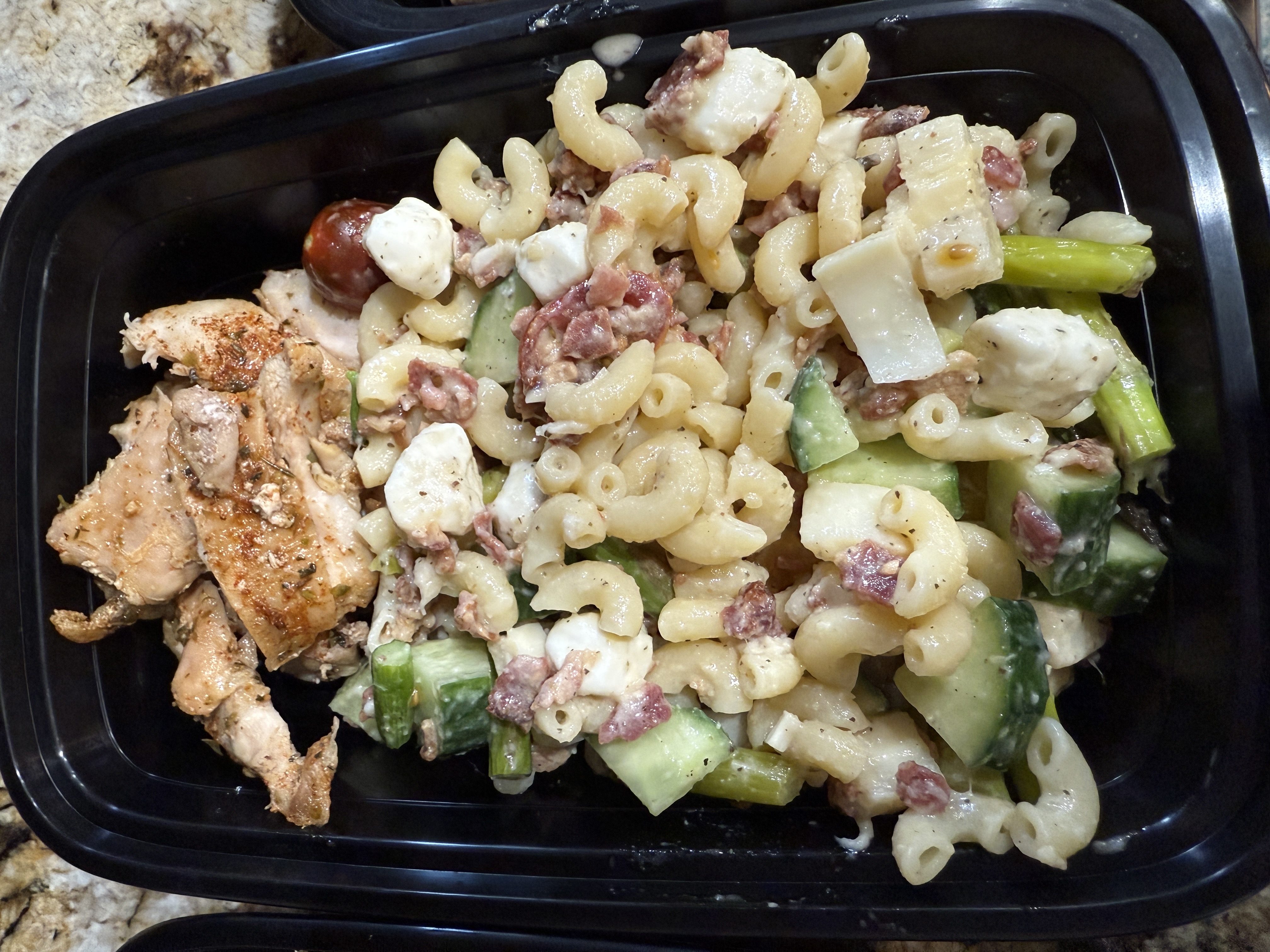 A portion of pasta salad mixed with vegetables and diced meat, served alongside pieces of seasoned grilled chicken.