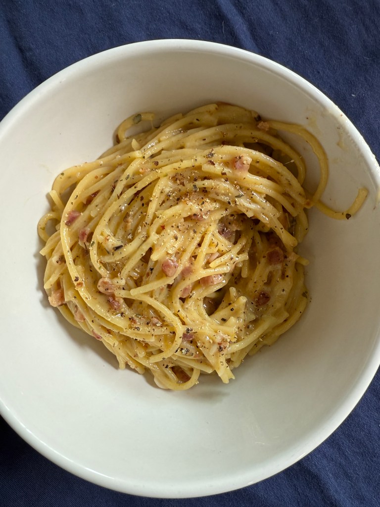 A bowl of spaghetti carbonara garnished with black pepper and bits of pancetta.