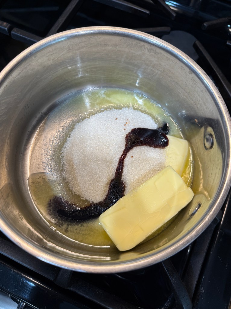 A saucepan on a stovetop containing melted butter, sugar, and molasses, ready for mixing.