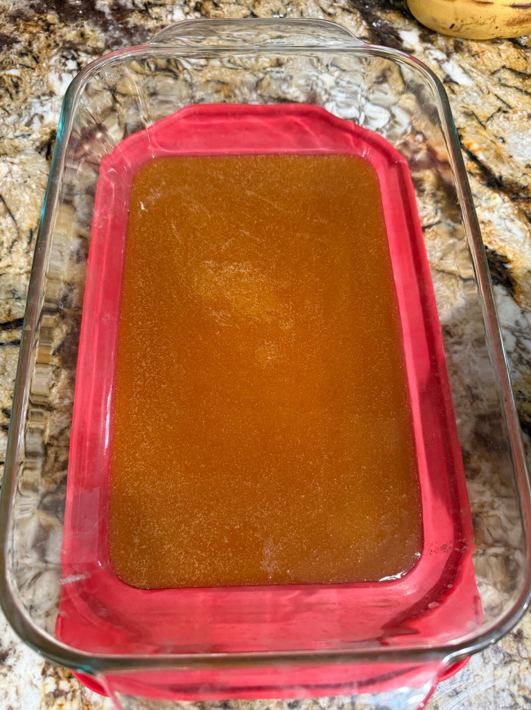 A glass baking dish with a brown liquid, likely a melted mixture of butter, sugar, and molasses, sitting on a granite countertop.
