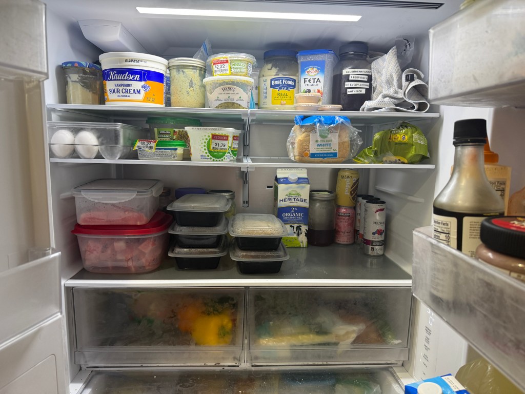 A well-stocked refrigerator with various containers of food, condiments, and beverages, showcasing a mix of leftovers, dairy products, and vegetables.