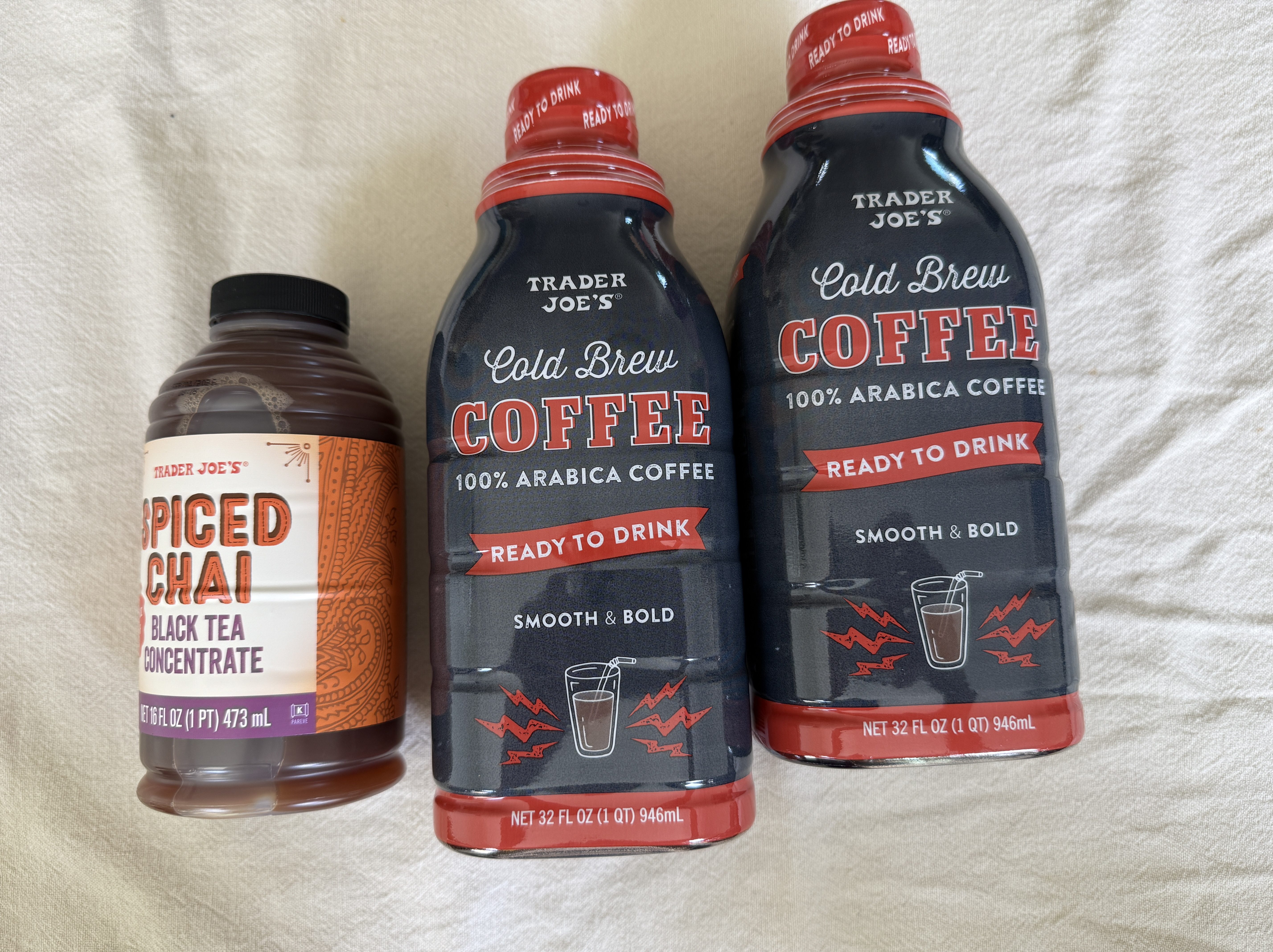 A bottle of spiced chai black tea concentrate next to two bottles of Trader Joe's cold brew coffee, all displayed on a light-colored surface.